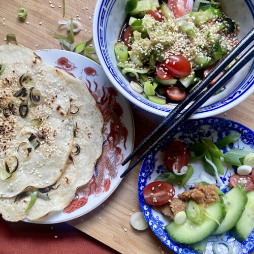 Delicious homemade savory pancake with crispy edges, topped with sesame seeds and served with a flavorful miso dipping sauce and a medley of chopped vegetables.