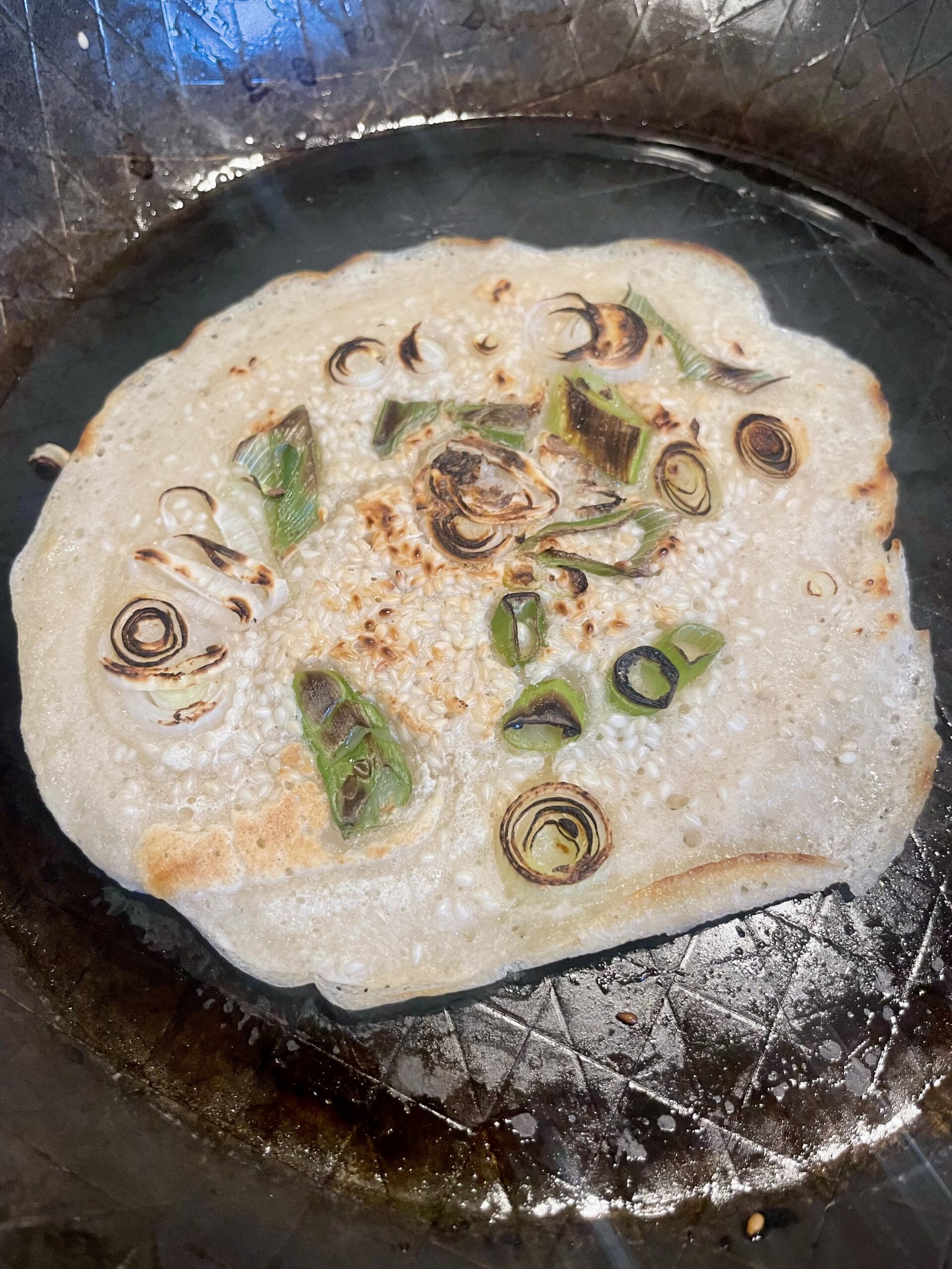 Cooking the savory pancake in a skillet over medium heat. Monitoring for the formation of small holes on the surface, indicating readiness for flipping. Adjusting heat to ensure even cooking without burning the edges.