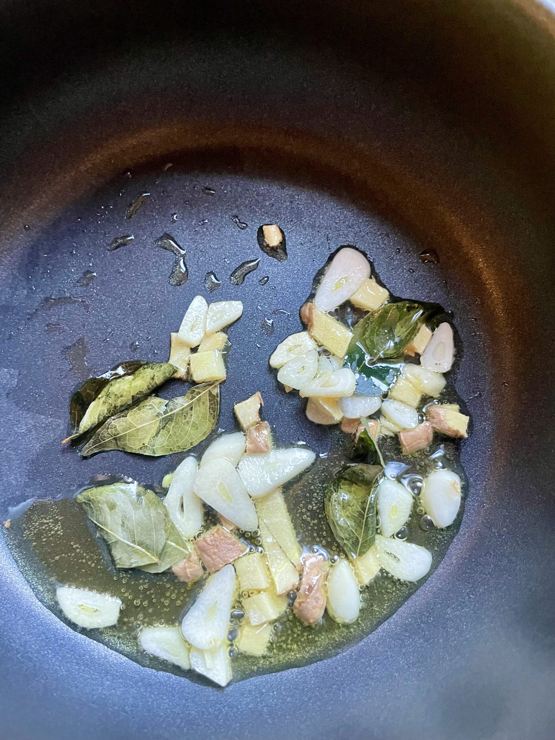 Sautéing curry leaves and garlic in warm olive oil for a burst of aromatic flavor. Quick and attentive cooking to avoid burning the garlic, requiring immediate removal from heat.