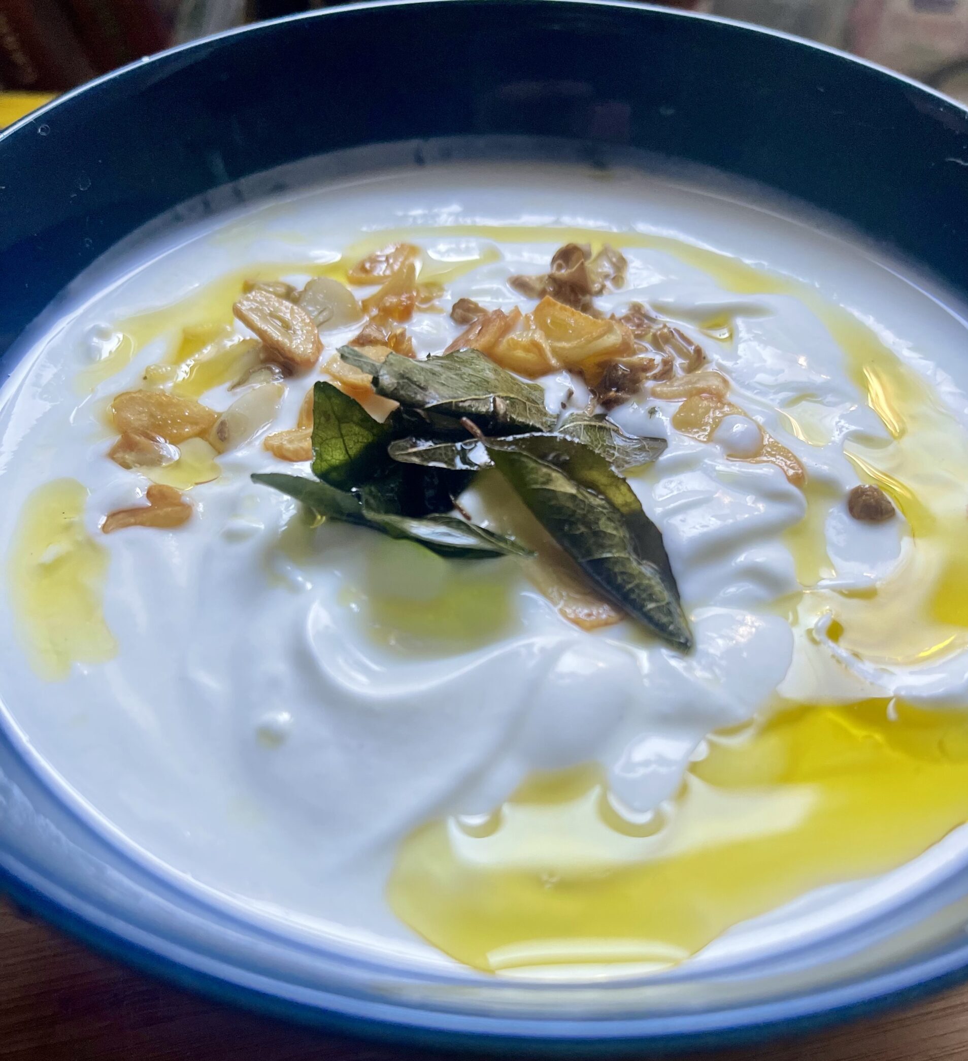 Close-up of my mom’s 3-ingredients Curry Leaf Raita (yogurt) featuring a vibrant curry leaf garnish and sautéed garlic, a delightful and aromatic Indian condiment.