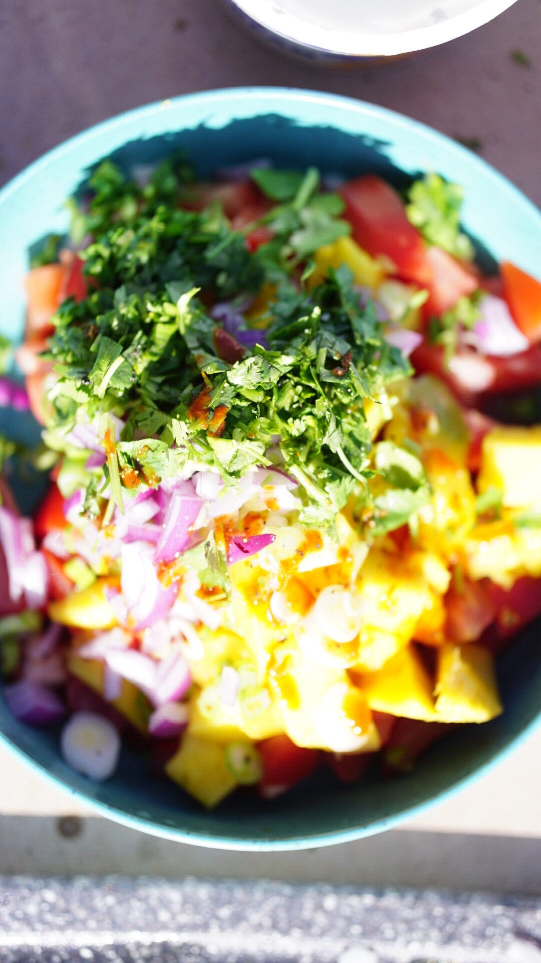 An appetizing summer salad titled 'Failsafe Summer Salad (Vegetarian & Camping-friendly)', consisting of diced tomatoes, red onions, ripe mango chunks, minced cilantro, and a creamy sour cream dressing, garnished with hot sauce and lemon juice. Perfect for outdoor adventures or potluck gatherings.