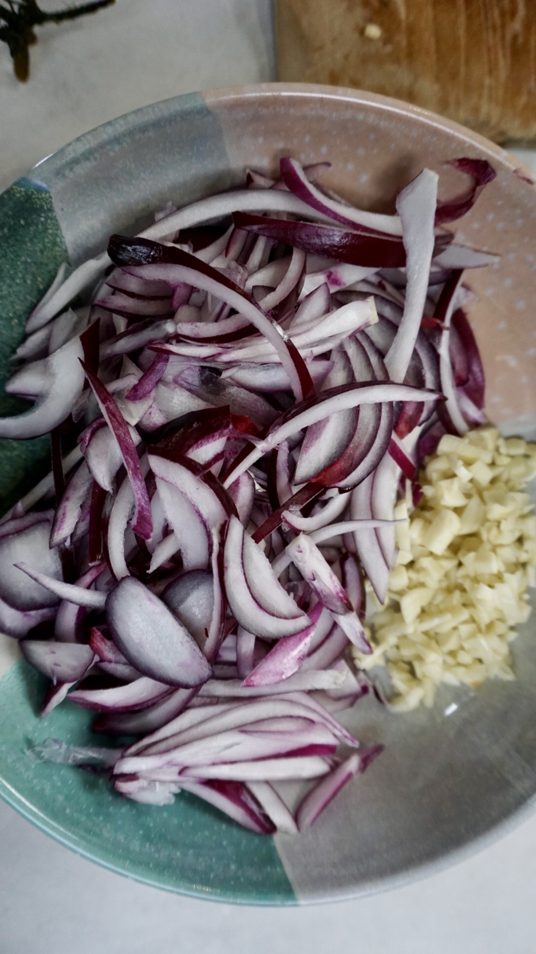 Freshly chopped garlic and onion on a plate, prepared to be sautéed with crispy tofu in a cooking pot.