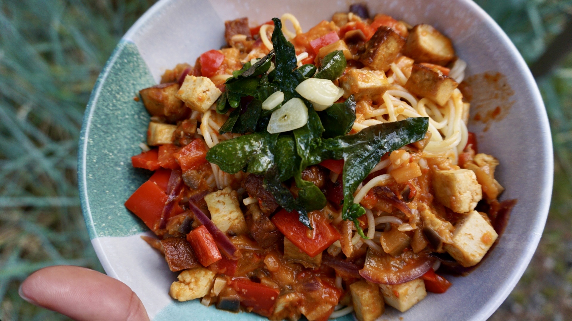 A plate of spaghetti topped with garlic sautéed bladderwrack algae, nestled in a rich ajvar sauce with crispy tofu and tender eggplant pieces. The dish is garnished with freshly ground black pepper, showcasing a colorful and nutritious meal.